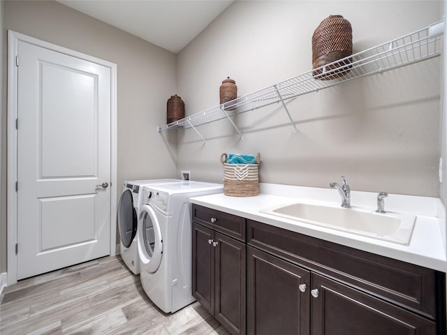 laundry area featuring separate washer and dryer, light wood-style flooring, a sink, and cabinet space