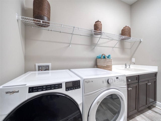 clothes washing area with light wood-type flooring, cabinet space, a sink, and independent washer and dryer