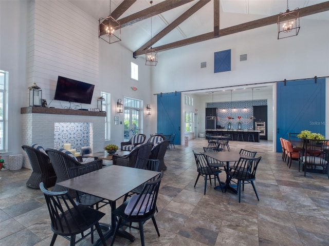 dining space with visible vents, lofted ceiling with beams, a barn door, stone finish flooring, and a chandelier