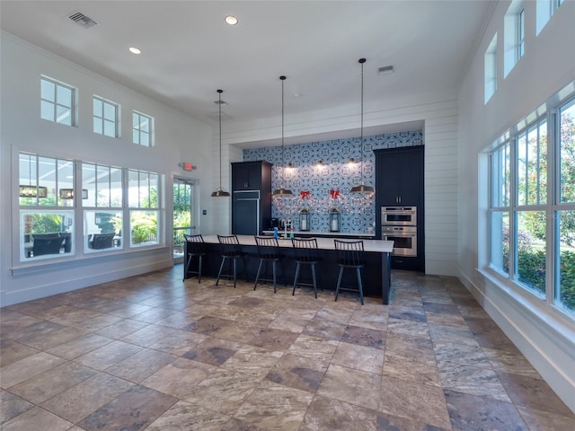 kitchen featuring decorative light fixtures, light countertops, visible vents, an island with sink, and a kitchen breakfast bar