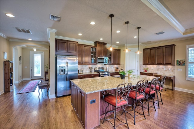 kitchen with a breakfast bar area, an island with sink, stainless steel appliances, and ornamental molding