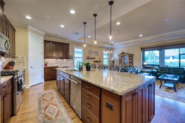 kitchen with a spacious island, sink, light hardwood / wood-style flooring, decorative light fixtures, and stainless steel appliances