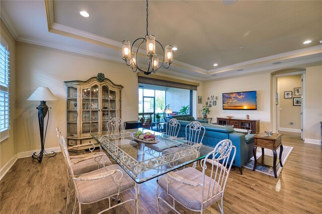 dining area featuring a raised ceiling, a chandelier, crown molding, and light hardwood / wood-style floors