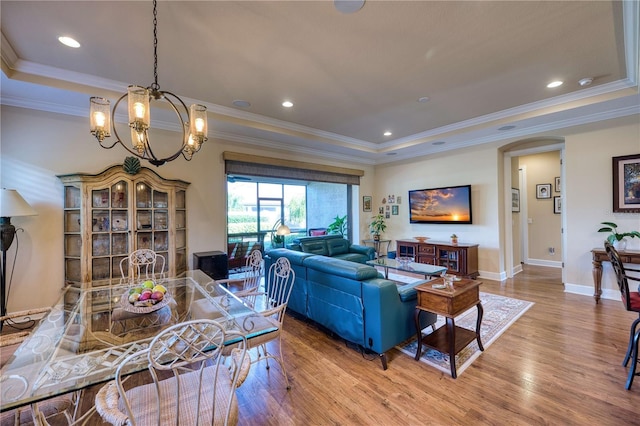 living room with a raised ceiling, an inviting chandelier, ornamental molding, and hardwood / wood-style flooring