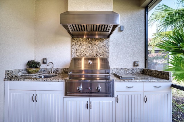 kitchen featuring stone countertops, white cabinetry, wall chimney exhaust hood, and sink