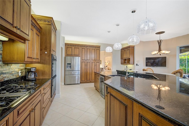 kitchen featuring backsplash, dark stone counters, stainless steel appliances, pendant lighting, and a chandelier