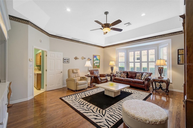 living room with hardwood / wood-style floors, a tray ceiling, ceiling fan, and ornamental molding