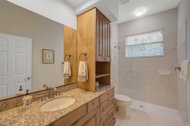 bathroom featuring a tile shower, tile patterned flooring, vanity, and toilet