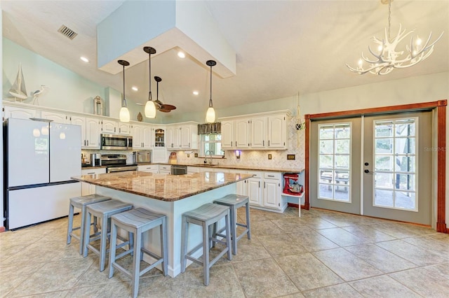 kitchen with a center island, hanging light fixtures, light stone counters, white cabinetry, and stainless steel appliances