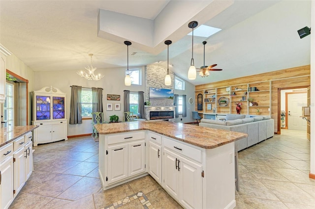 kitchen with light stone counters, built in shelves, ceiling fan with notable chandelier, white cabinets, and a kitchen island