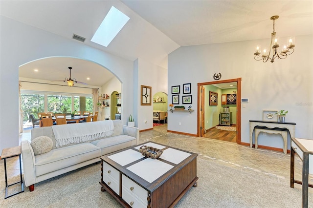 living room with vaulted ceiling with skylight and ceiling fan with notable chandelier