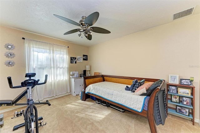 bedroom with ceiling fan, light colored carpet, and a textured ceiling