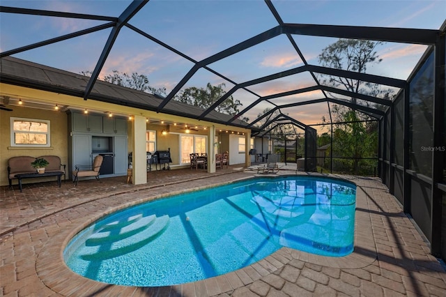 pool at dusk with area for grilling, glass enclosure, ceiling fan, and a patio area