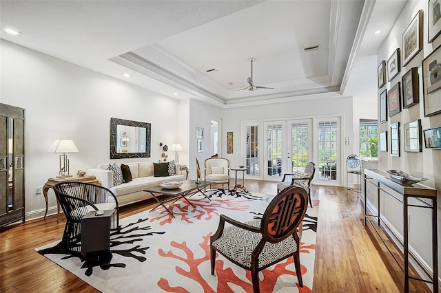 living room featuring ceiling fan, french doors, light hardwood / wood-style flooring, a tray ceiling, and ornamental molding