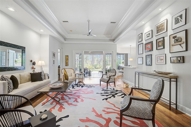 living room with a tray ceiling, ceiling fan, light hardwood / wood-style floors, and ornamental molding