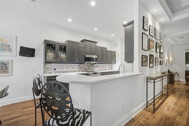 kitchen with stainless steel appliances, tasteful backsplash, dark hardwood / wood-style floors, kitchen peninsula, and ornamental molding