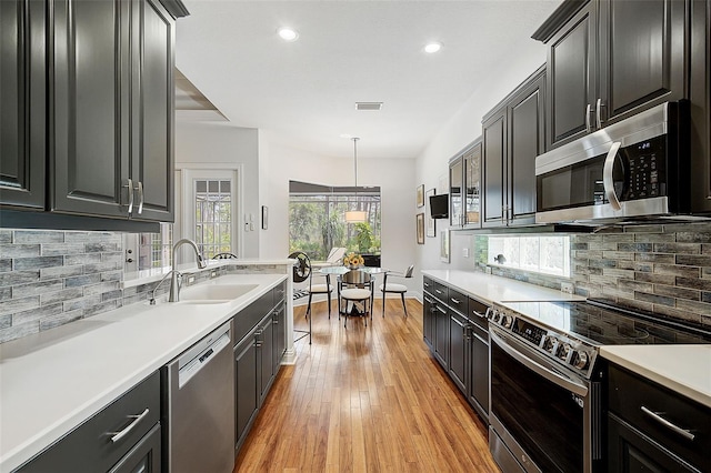 kitchen with decorative backsplash, stainless steel appliances, sink, light hardwood / wood-style floors, and hanging light fixtures