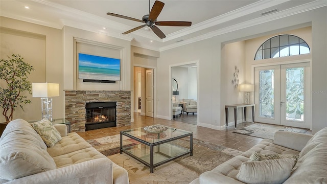 living room featuring ceiling fan, a stone fireplace, crown molding, and french doors