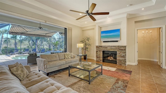 living room featuring ceiling fan, a raised ceiling, crown molding, a fireplace, and light tile patterned floors