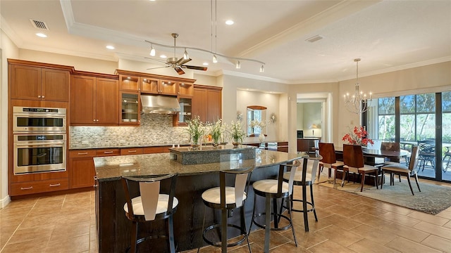 kitchen with stainless steel double oven, tasteful backsplash, pendant lighting, dark stone counters, and a kitchen bar