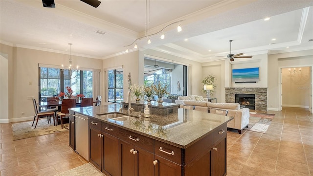 kitchen featuring a raised ceiling, light stone counters, sink, and an island with sink