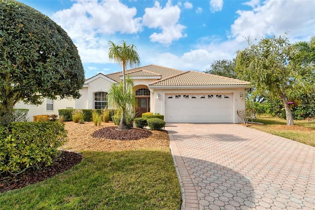 mediterranean / spanish-style house with a tile roof, an attached garage, decorative driveway, a front lawn, and stucco siding