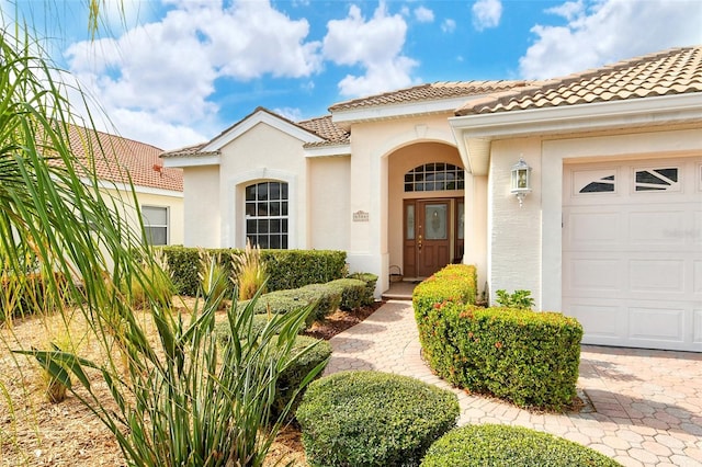 doorway to property featuring an attached garage, a tile roof, and stucco siding