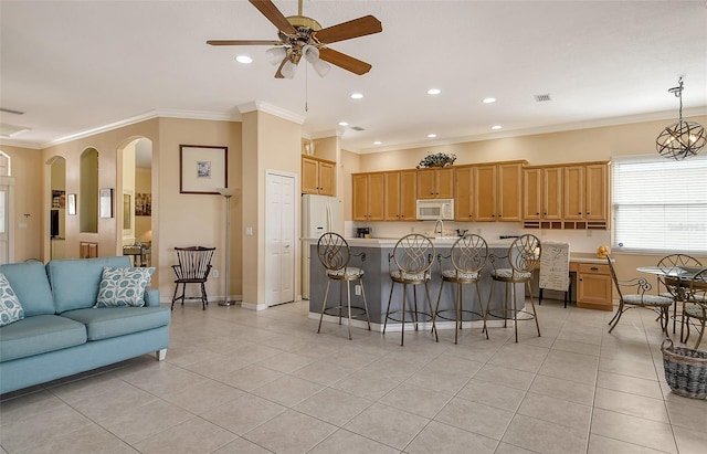 kitchen with white appliances, an island with sink, ornamental molding, a breakfast bar, and light countertops