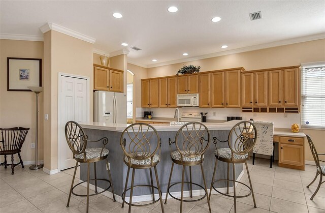 kitchen featuring white appliances, a kitchen island with sink, light countertops, and crown molding