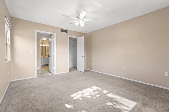 unfurnished bedroom with connected bathroom, ceiling fan, a closet, and light colored carpet