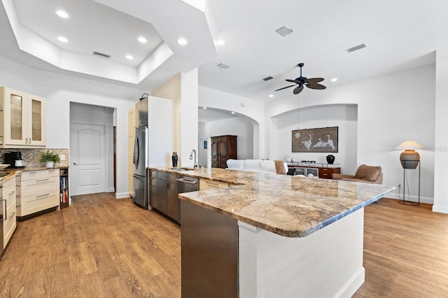 kitchen featuring kitchen peninsula, light stone countertops, stainless steel appliances, ceiling fan, and sink