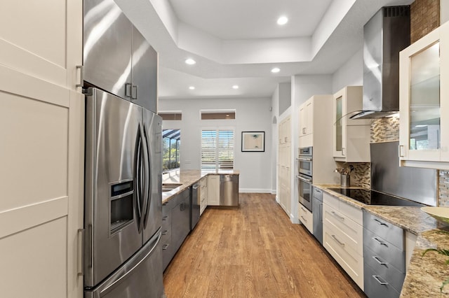 kitchen with light stone countertops, backsplash, wall chimney exhaust hood, stainless steel appliances, and white cabinets