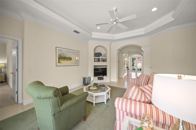 living room with light tile patterned flooring, built in features, crown molding, and a tray ceiling