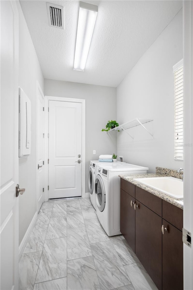 washroom featuring cabinets, sink, a textured ceiling, and washing machine and clothes dryer