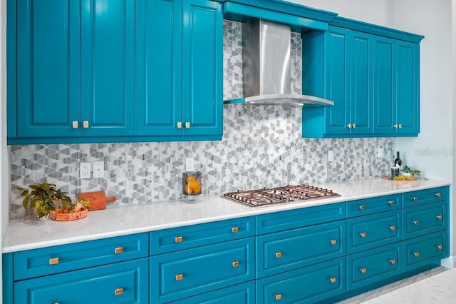 kitchen with decorative backsplash, wall chimney range hood, stainless steel gas cooktop, and blue cabinets