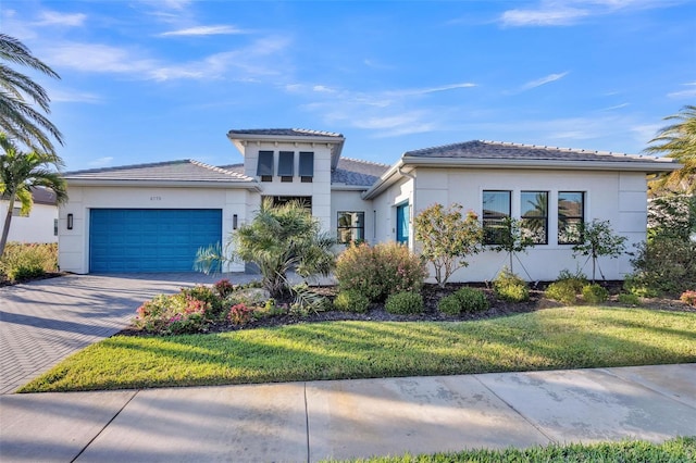 prairie-style home with stucco siding, an attached garage, a front yard, and decorative driveway