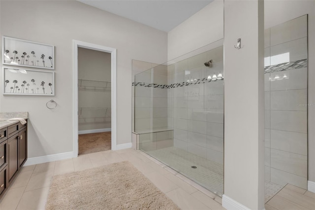 bathroom featuring a walk in shower, baseboards, tile patterned flooring, vanity, and a walk in closet