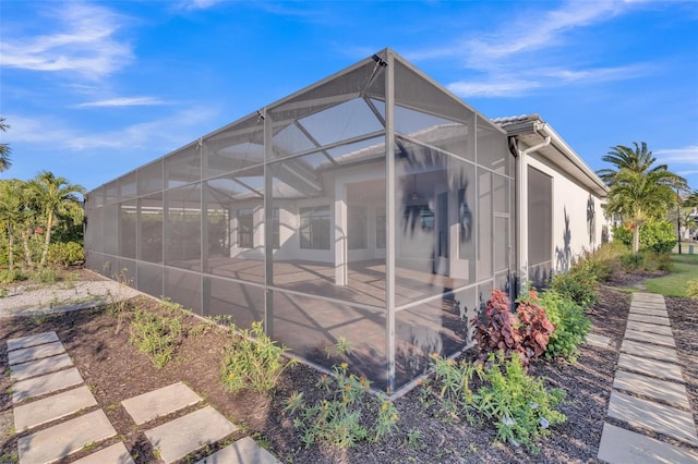 rear view of house featuring glass enclosure, a patio area, and stucco siding