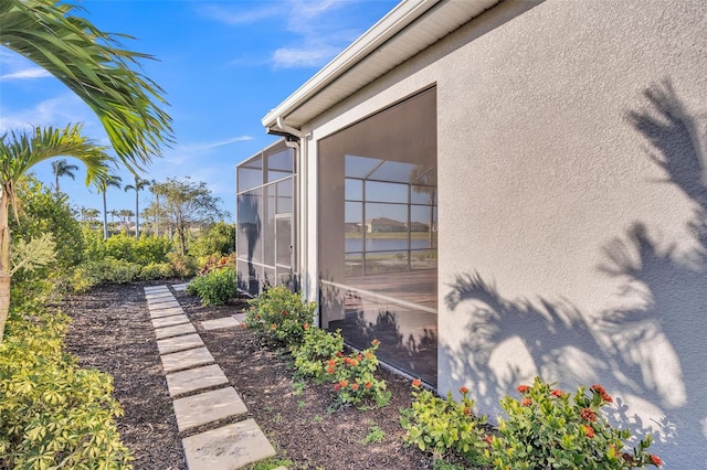 view of side of home with glass enclosure and stucco siding