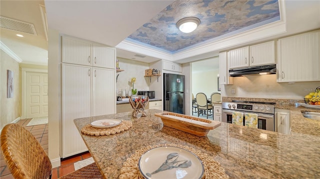 kitchen with a raised ceiling, light stone countertops, stainless steel range oven, ornamental molding, and black refrigerator