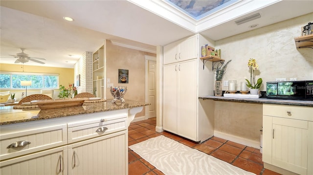 kitchen featuring tile patterned flooring, dark stone countertops, built in features, cream cabinets, and ceiling fan