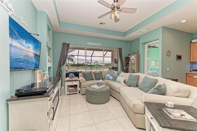 living room featuring a tray ceiling, ceiling fan, and light tile patterned floors