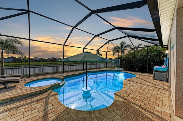 pool at dusk featuring glass enclosure, a patio area, and an in ground hot tub