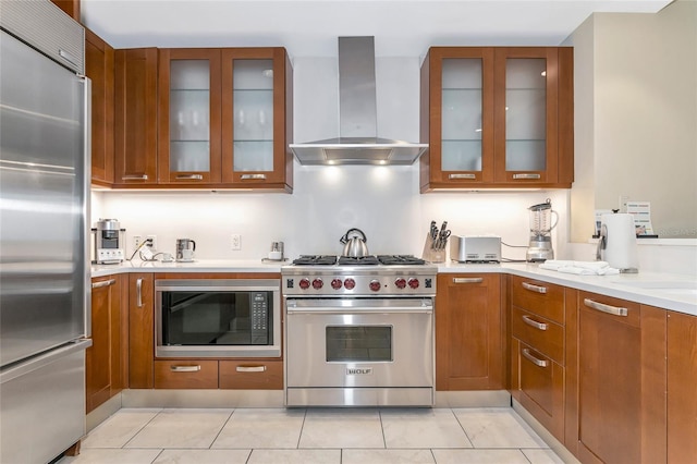 kitchen with light stone countertops, light tile patterned floors, built in appliances, and wall chimney range hood