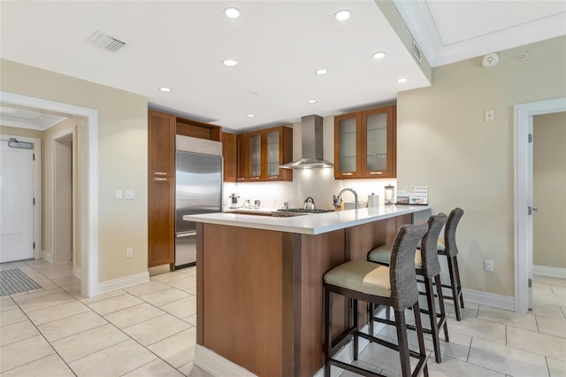 kitchen featuring kitchen peninsula, a breakfast bar, stainless steel appliances, crown molding, and wall chimney range hood