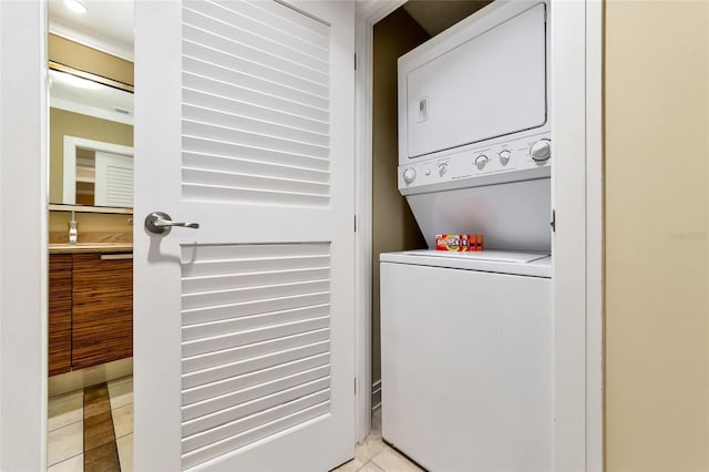 clothes washing area with stacked washing maching and dryer, crown molding, and light tile patterned floors