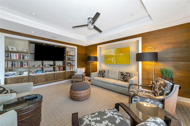 living room featuring ornamental molding, a tray ceiling, ceiling fan, built in features, and wood walls