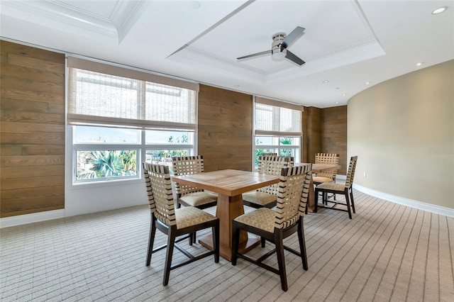 carpeted dining room with a tray ceiling, ceiling fan, ornamental molding, and wood walls