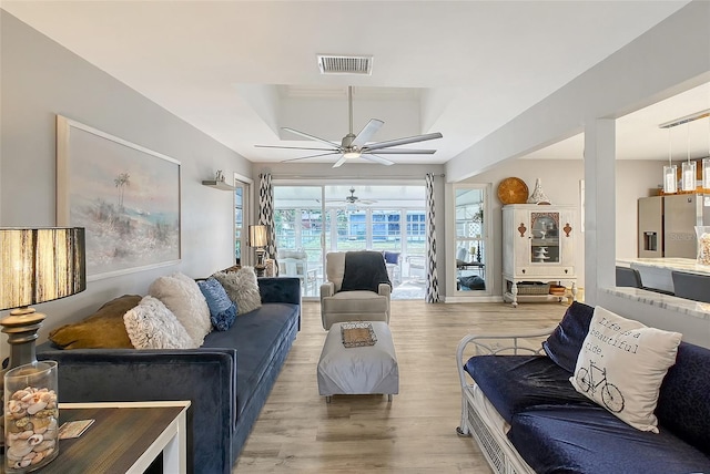 living room featuring a raised ceiling, ceiling fan, and light hardwood / wood-style floors