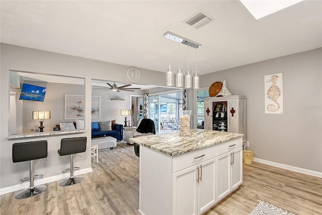 kitchen with light stone counters, ceiling fan, pendant lighting, white cabinets, and a center island